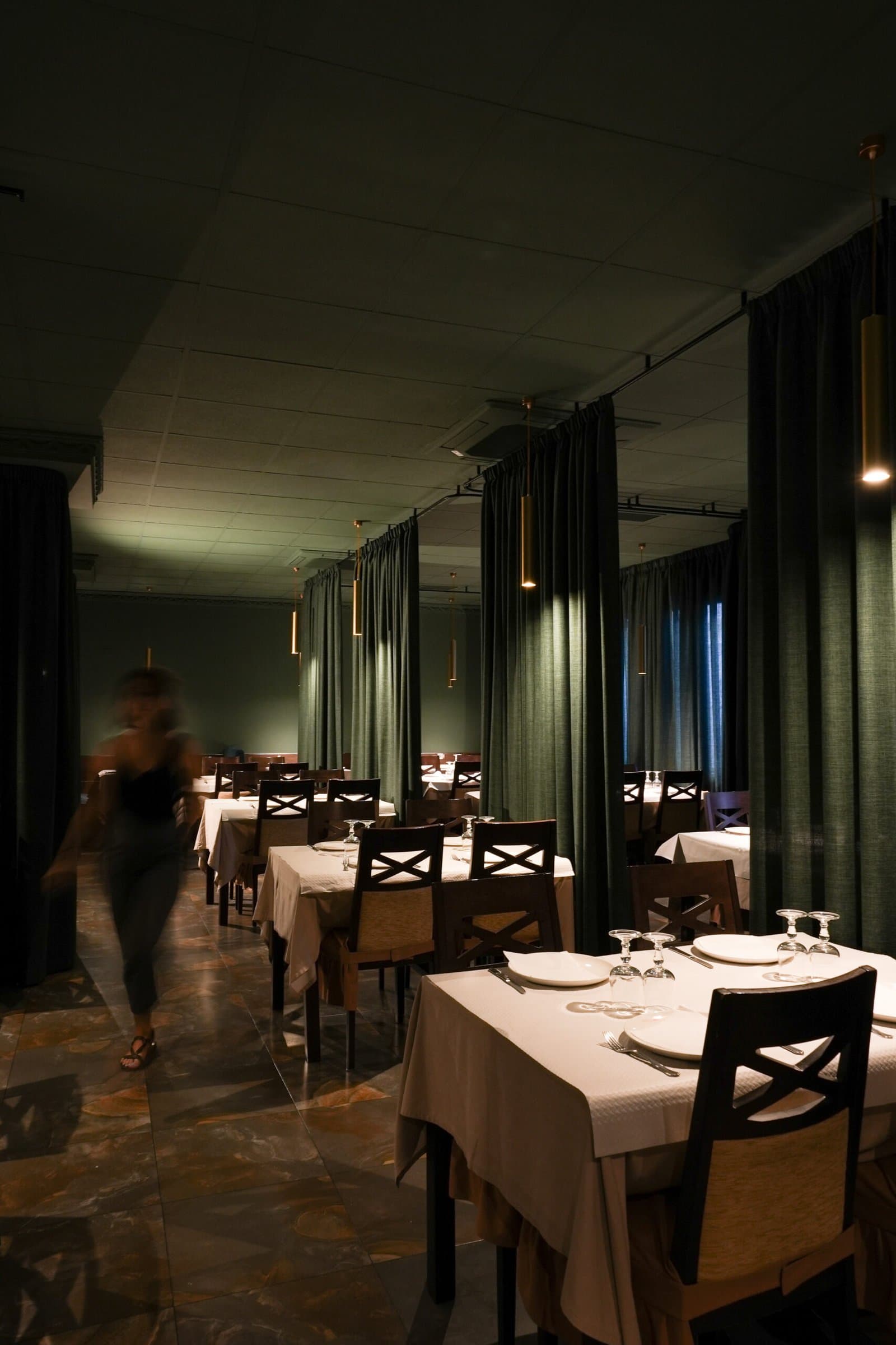 Restaurant interior with green curtains, dark wooden chairs and set tables