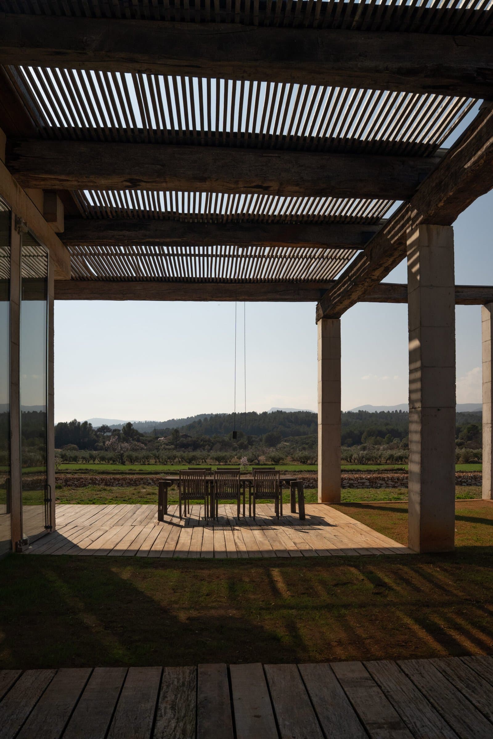 Covered terrace with a slatted pergola, dining table and views over the fields