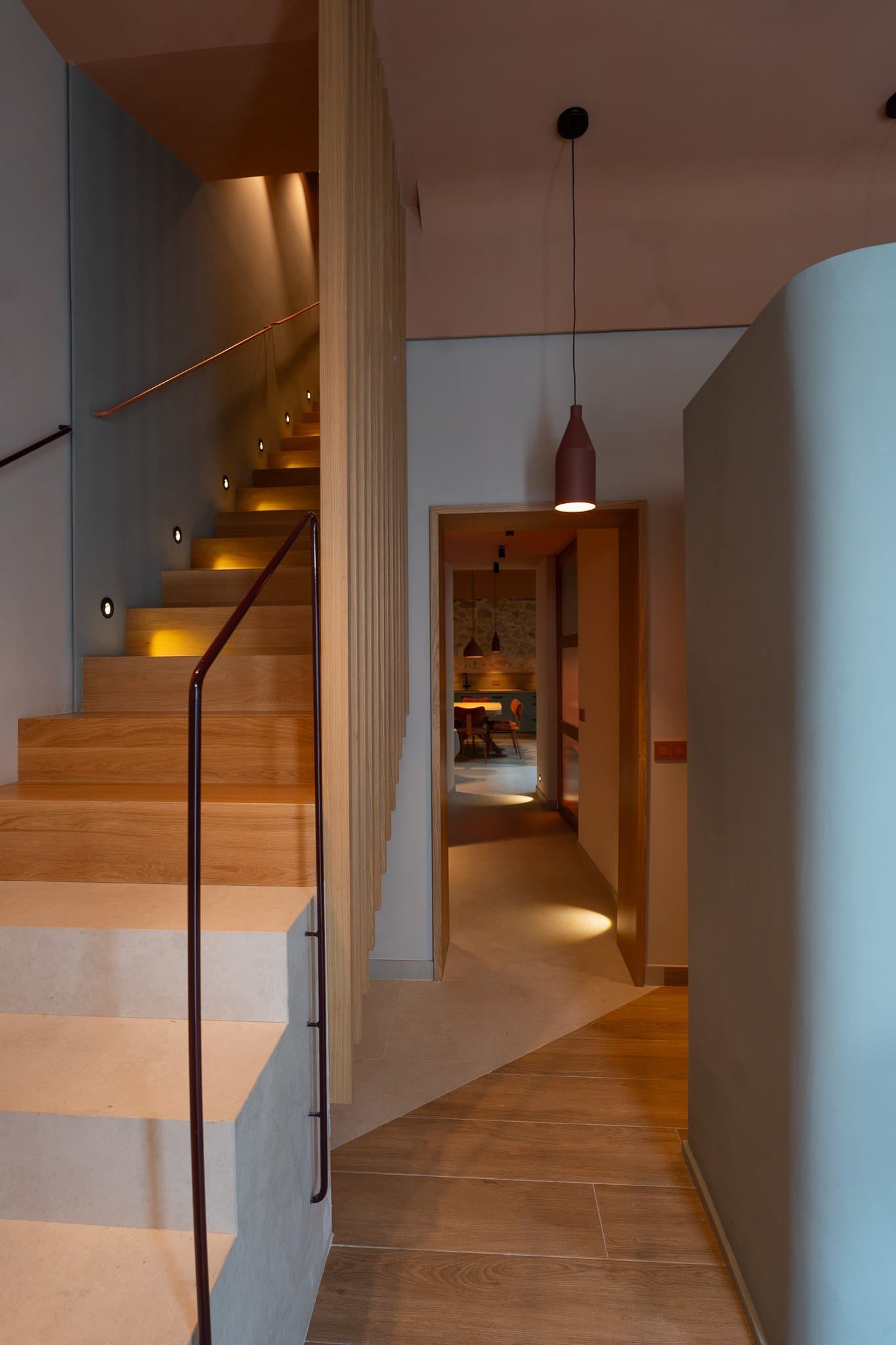 Wooden stairs leading to a curved corridor with indirect lighting