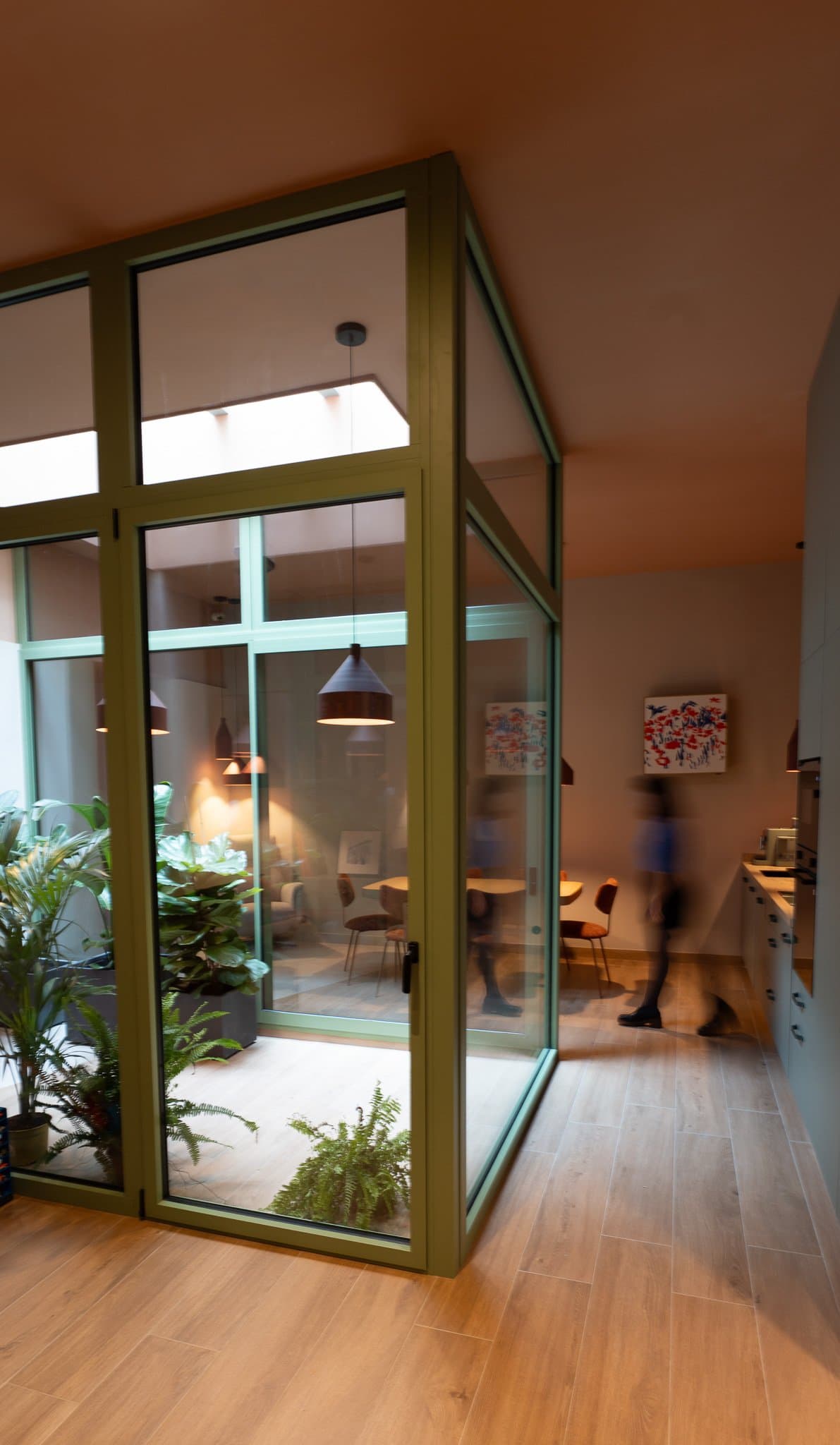 Green-framed glass room with an indoor garden, seen from the hallway