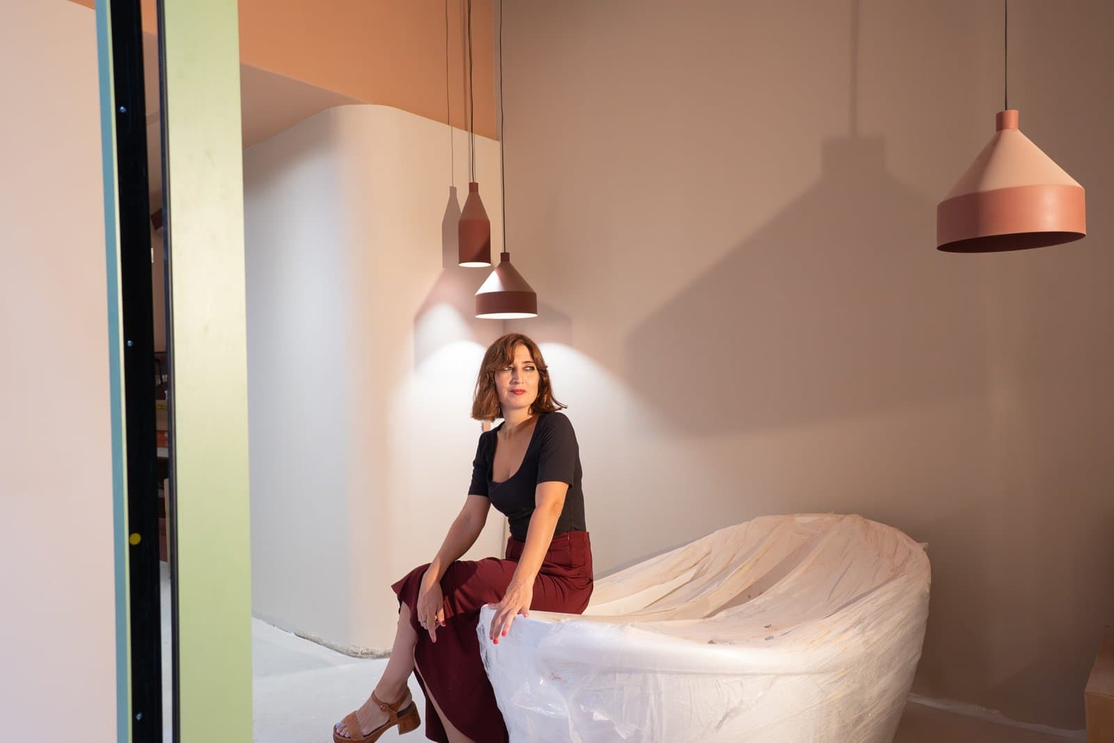 Woman seated on a curved white sofa under terracotta pendant lamps
