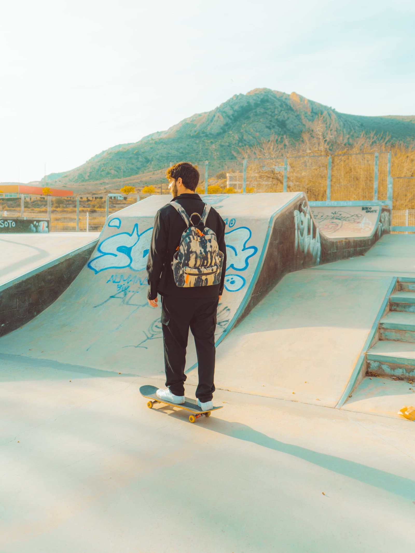 Skateboarder seen from behind carrying a backpack at a skatepark