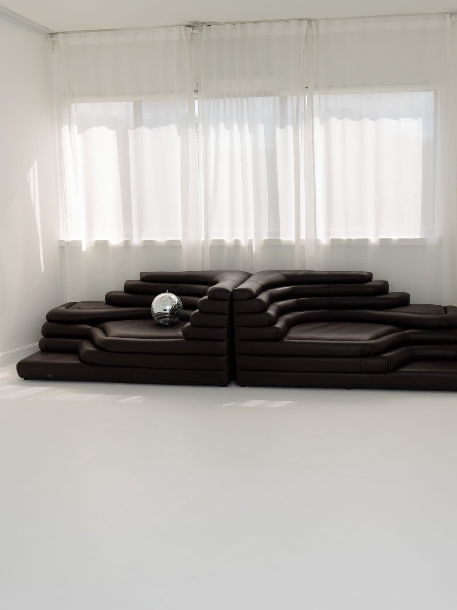 Studio with a dark brown modular leather sofa against white curtains