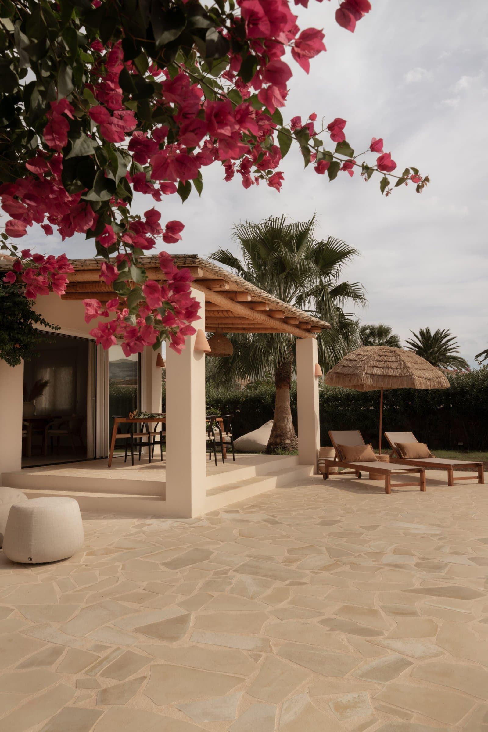 Terrace under flowering bougainvillea with a pergola, loungers and stone paving