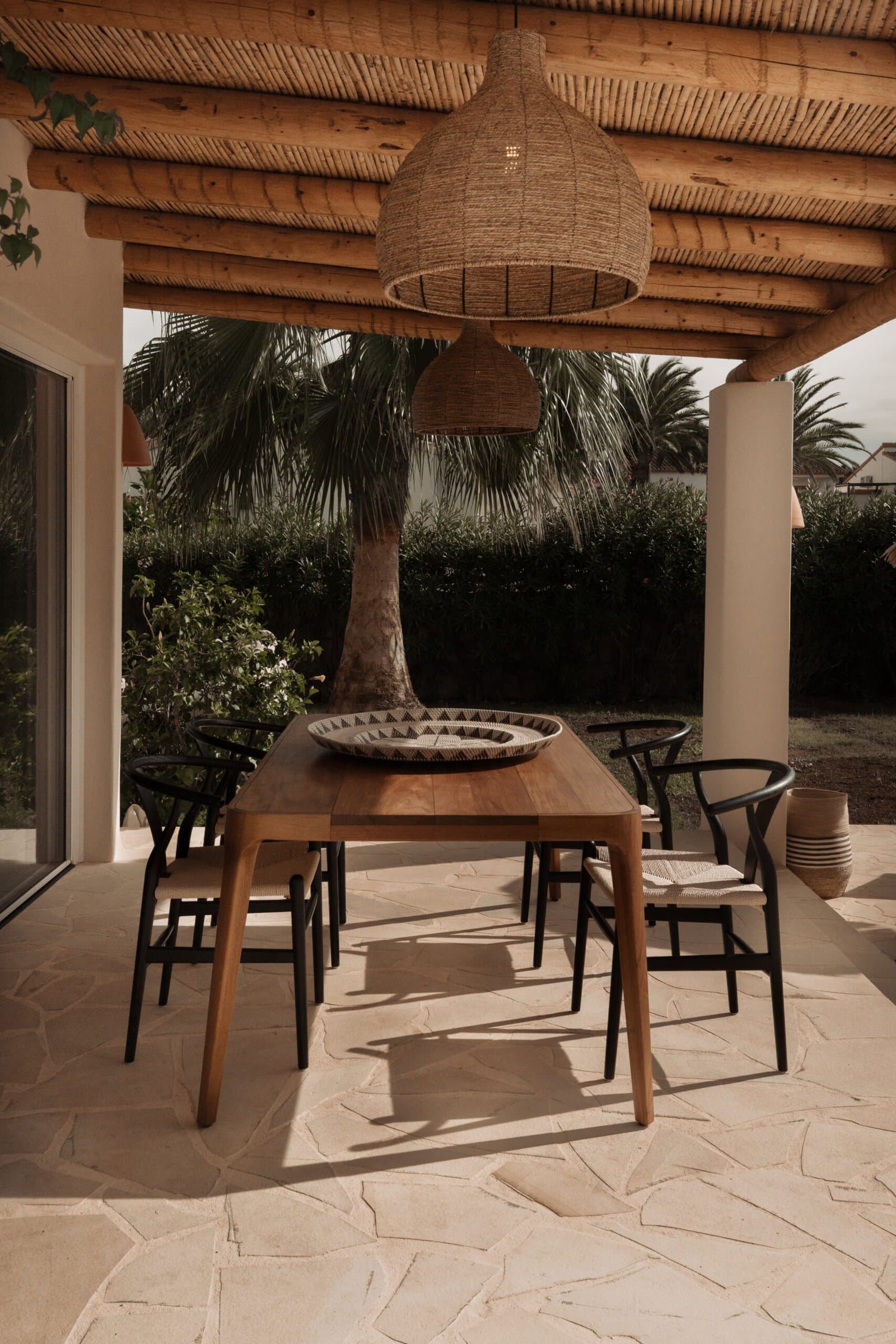 Outdoor dining table under a cane pergola with a large woven lamp