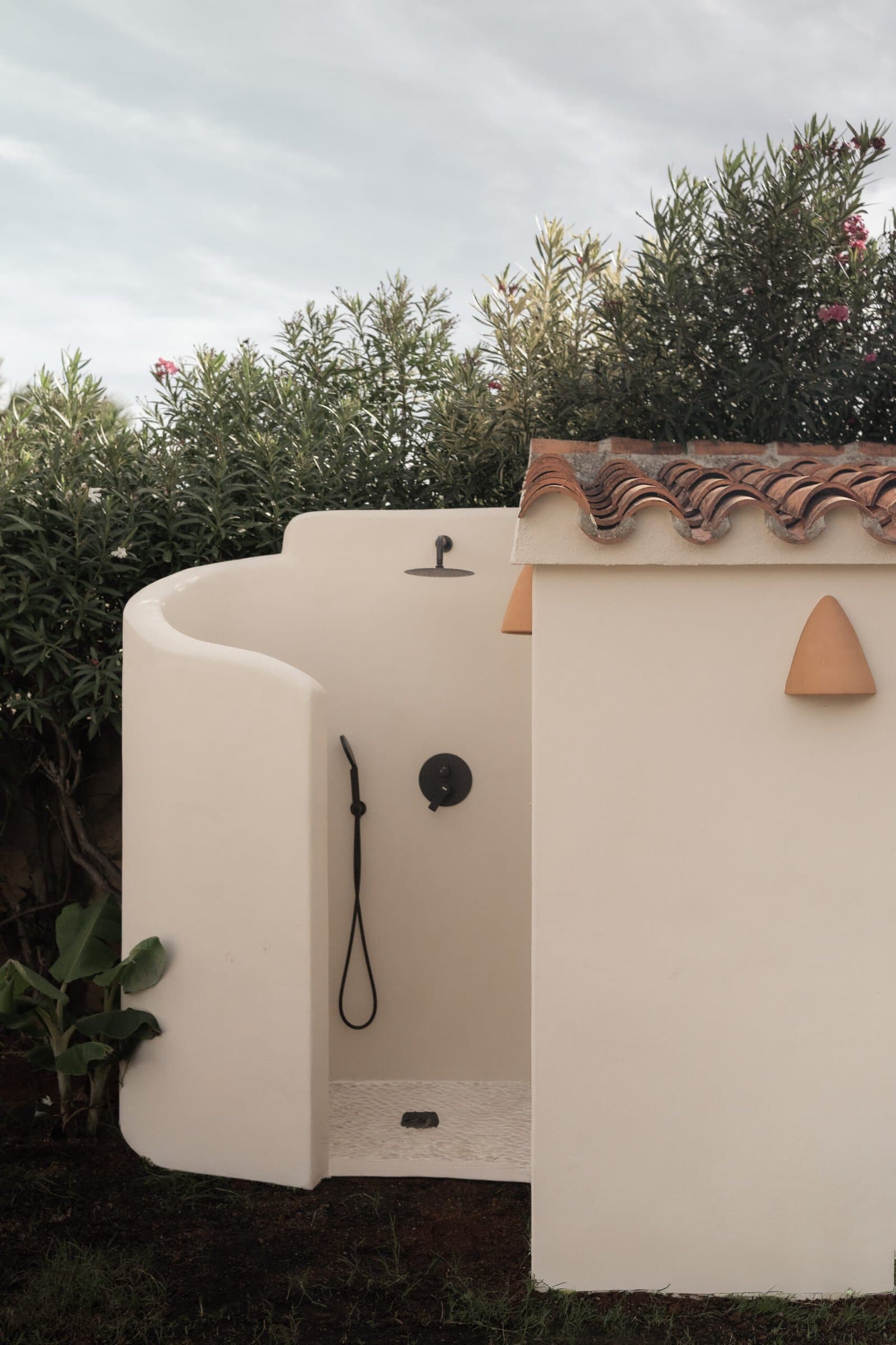 Curved whitewashed outdoor shower among the garden plants