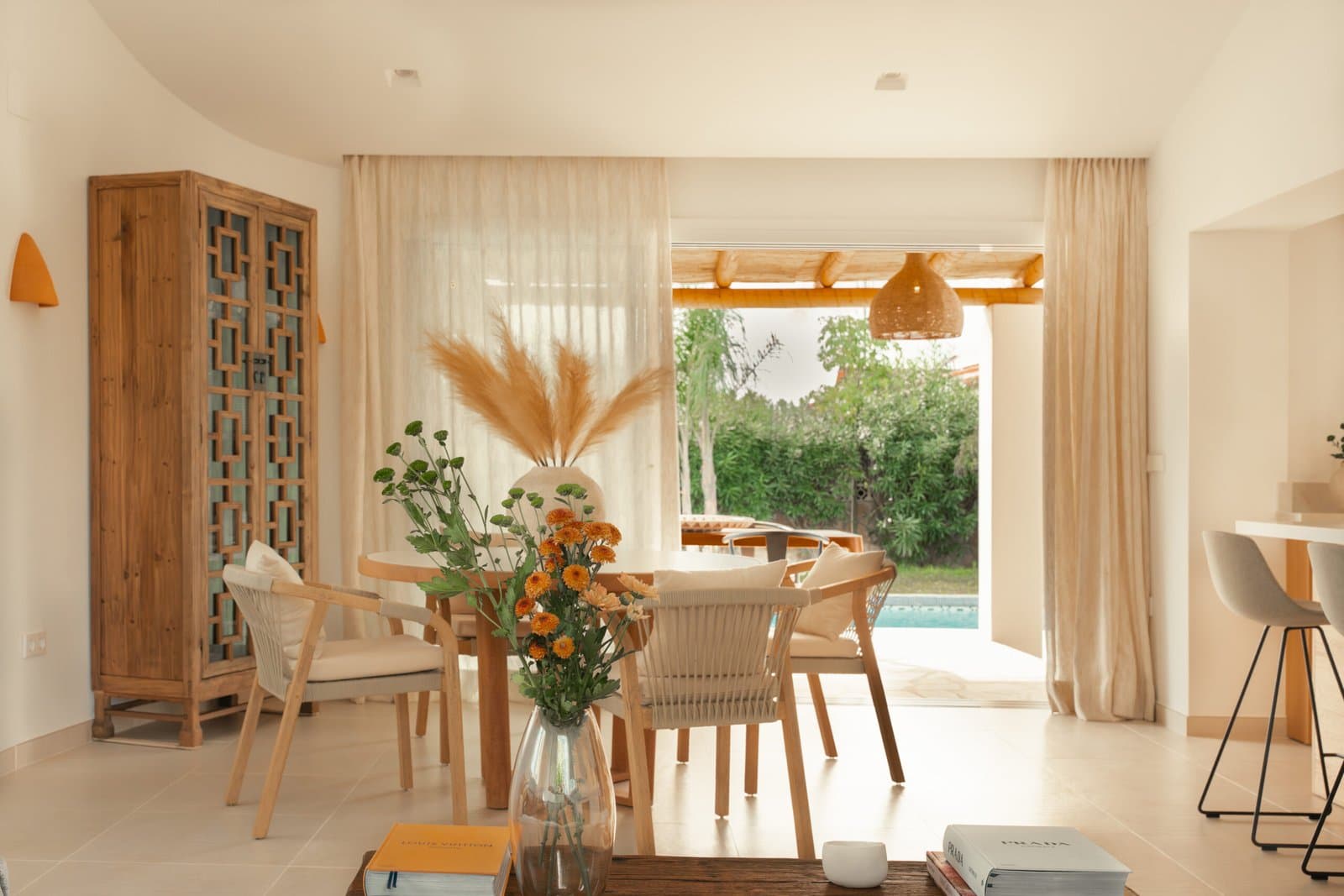 Dining room opening onto the pool, with a carved wooden cabinet and flowers