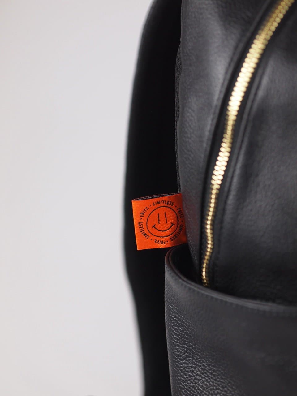 Detail of a black leather backpack with a gold zip and the orange label