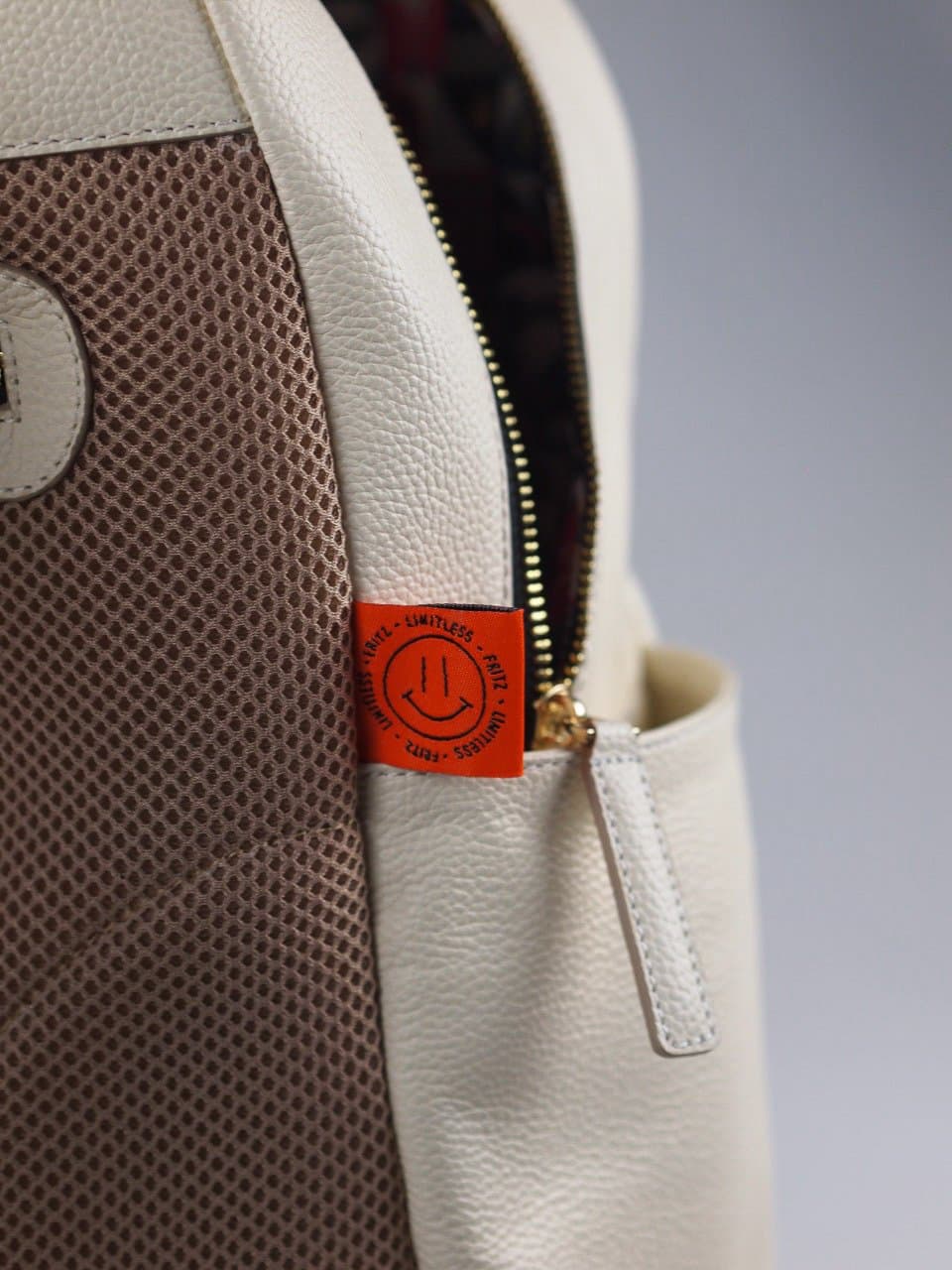 Detail of the zip and orange brand label on a cream leather backpack