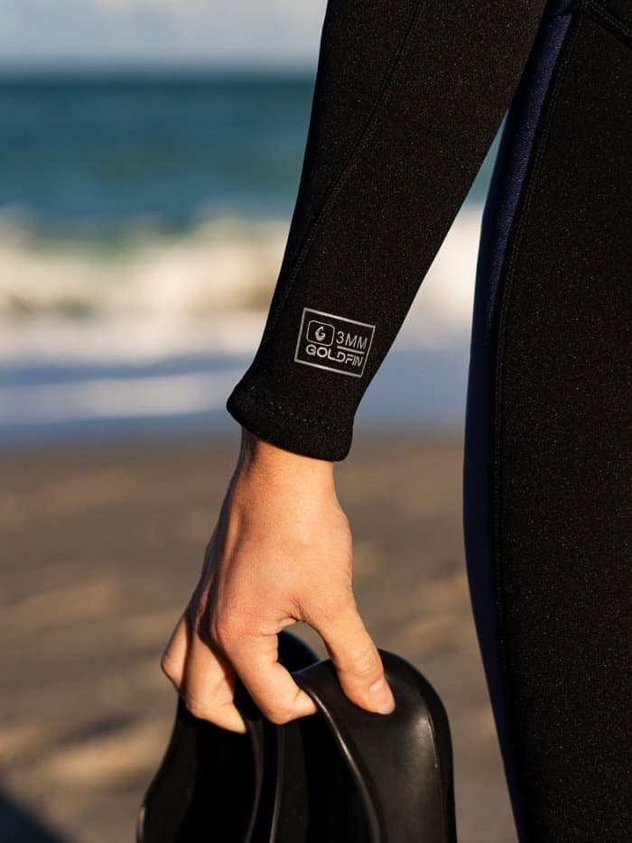 Hand holding fins beside the leg of a wetsuit marked 3MM
