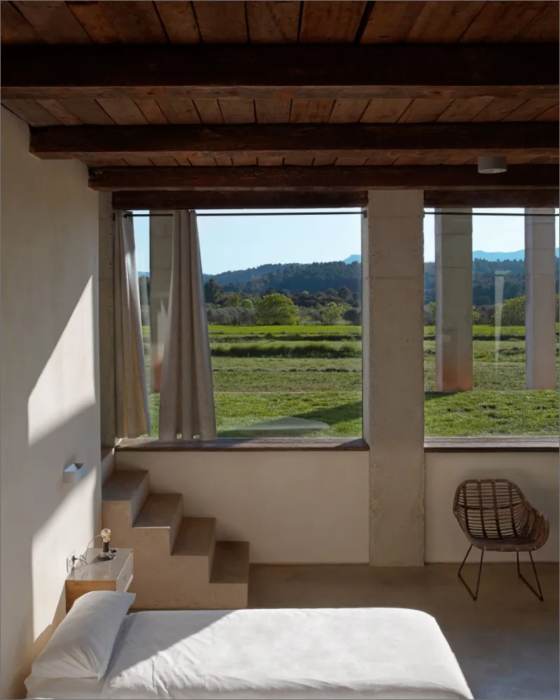 Bedroom with large windows onto green fields and a bed in the foreground